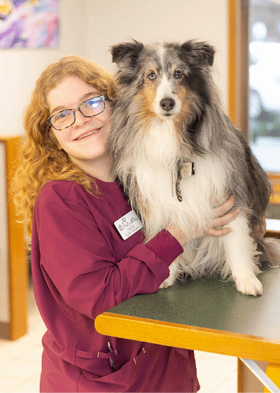 Chezni female with long strawberry blonde hair wearing glasses and posing with a Sheltie