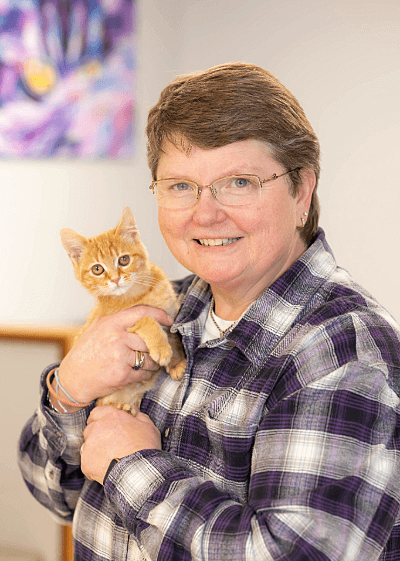 Mary female with pixie cut and glasses wearing a plaid long sleeve shirt holding an orange and white kitten